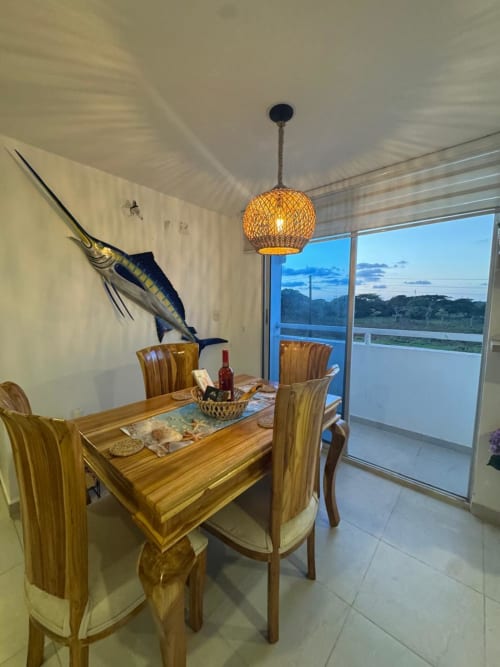 Comedor moderno del apartamento Olamar Living en Santiago de Tolú con mesa de madera, lámpara colgante tejida y arte de pez vela