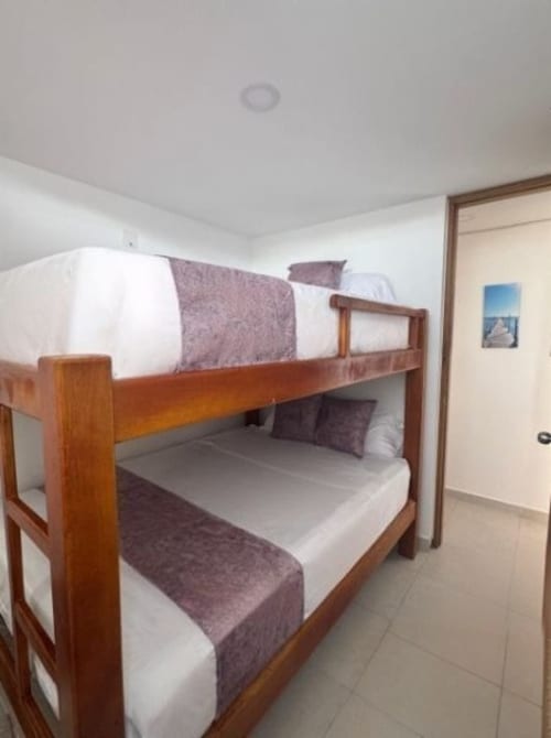 Cama litera con estructura de madera y ropa de cama blanca y púrpura en el dormitorio del apartamento de Olamar Living, Santiago de Tolú
