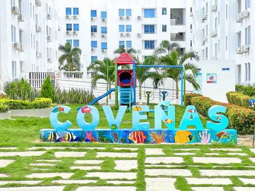 Colorido letrero COVEÑAS con parque infantil y palmeras en el hotel-apartamentos Olamar Living en Santiago de Tolú, Colombia