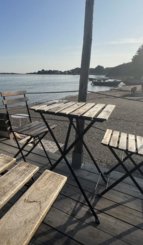 Zone de restauration en bord de mer aux Gîtes De L'odet avec chaises et table en bois face à l'estuaire de l'Odet à Clohars-Fouesnant,