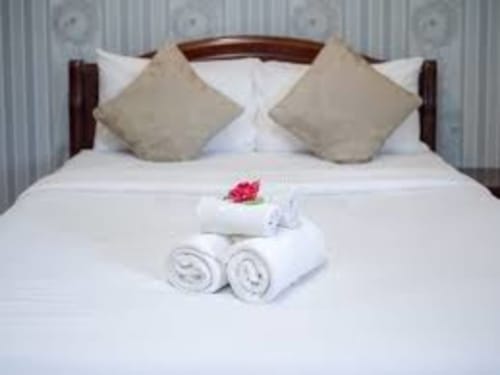 Lit élégamment présenté à Vacances en Touraine avec coussins décorés, serviettes roulées et une fleur rose
