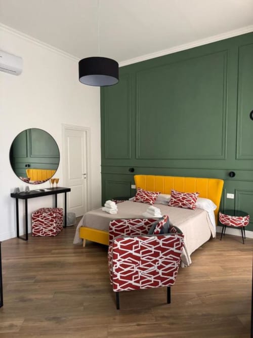 Modern bedroom at Le Boutique del Centro Naples with yellow bed, green wall paneling, patterned red cushions, and circular