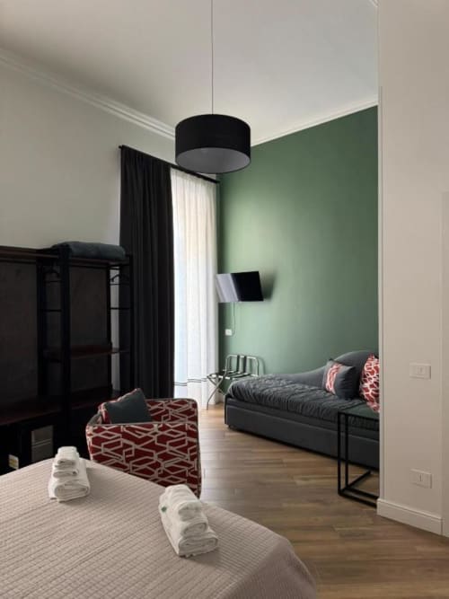 Modern bedroom at Le Boutique del Centro Naples with green accent wall, black bed, red geometric ottoman, and city view