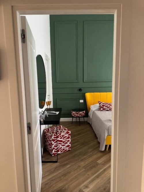 Modern bedroom at Le Boutique del Centro in Naples with green accent wall, yellow headboard, and patterned cushions