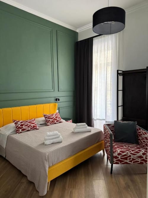 Modern bedroom at Le Boutique del Centro in Naples with yellow bed, green paneled walls, and city views from balcony