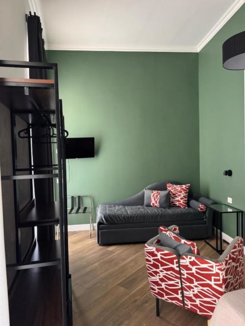 Modern bedroom at Le Boutique del Centro in Naples with green walls, gray daybed, red patterned chairs, and wooden floors