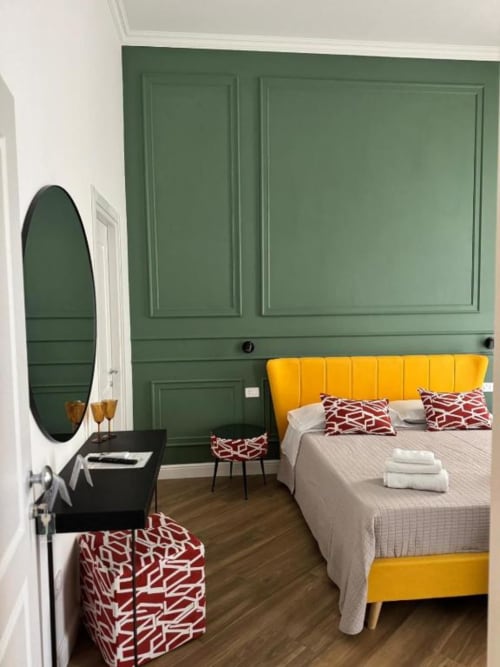 Modern hotel bedroom at Le Boutique del Centro in Naples with yellow bed, green paneled walls, and city view mirror