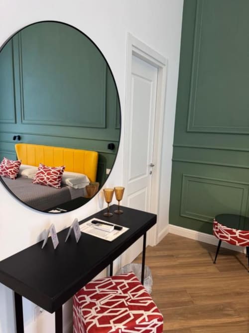 Modern hotel room at Le Boutique del Centro in Naples with green walls, yellow headboard, round mirror, black desk, and red