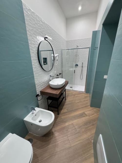 Modern bathroom at Le Boutique del Centro in Naples featuring teal tiles, vessel sink, round mirror, walk-in shower, and