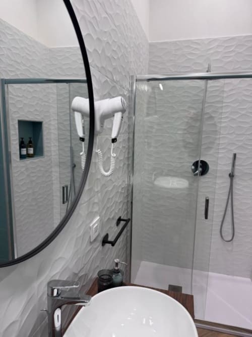 Modern bathroom at Le Boutique del Centro in Naples with white textured tile walls, walk-in shower, white sink, and black