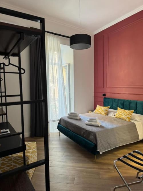 Modern bedroom at Le Boutique del Centro Naples with green headboard, yellow pillows, red accent wall, and balcony access