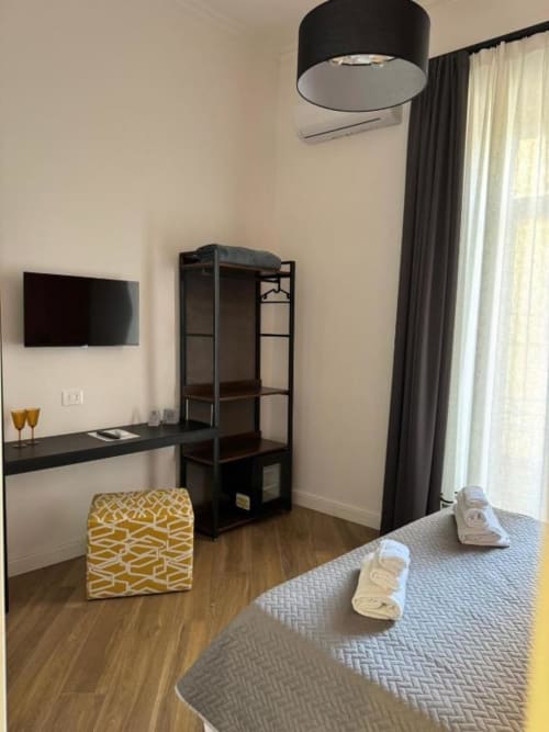 Modern hotel room at Le Boutique del Centro in Naples with bed, desk, TV, shelving, black pendant lamp, and balcony view