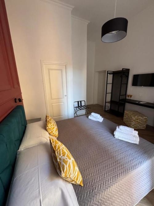 Modern bedroom at Le Boutique del Centro in Naples with bed, yellow pillows, TV, black pendant lamp, and white towels on bed