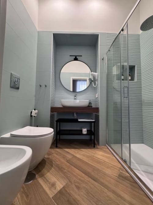 Modern bathroom at Le Boutique del Centro in Naples featuring white toilet, round mirror, vessel sink on wooden counter, and