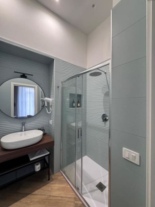 Modern bathroom at Le Boutique del Centro in Naples with rainfall shower, round mirror, and seafoam green tilework