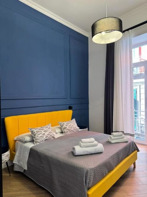 Camera moderna al Le Boutique del Centro Napoli con letto giallo, parete in blu navy, lampada a sospensione e vista sulla città dal balcone