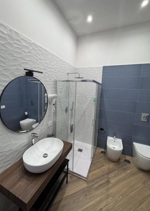 Bagno moderno presso Le Boutique del Centro, Napoli con piastrelle bianche texturizzate, parete accent scura, specchio ovale, lavabo a vessel e