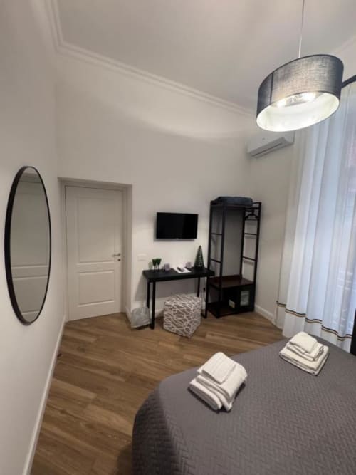 Camera moderna a Le Boutique del Centro a Napoli con letto, scrivania, specchio nero, TV, lampada a sospensione e pavimento in legno