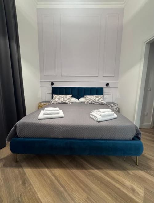 Camera moderna presso Le Boutique del Centro a Napoli con letto rivestito in azzurro scuro, biancheria grigia e cuscini bianchi