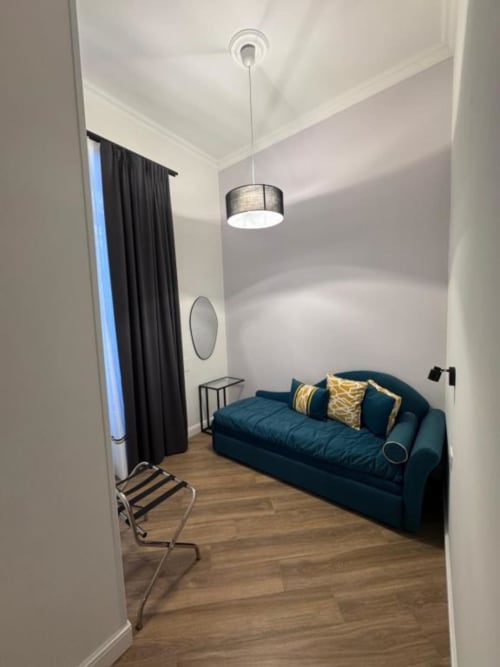 Daybed color teal con cuscini dorati in camera moderna del Le Boutique del Centro di Napoli, con lampada a sospensione e tende con vista sulla città