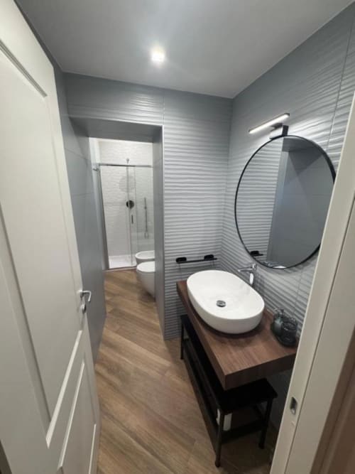 Bagno moderno con specchio ovale, lavabo bianco, mobile in legno e pareti piastrellate grigie presso Le Boutique del Centro, Napoli