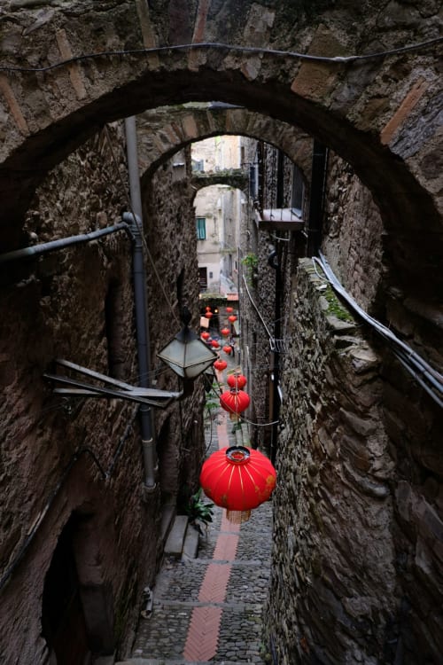 Strettissimo vicolo lastricato a Dolceacqua con lanterne rosse e archi in pietra, Agritusmo Stecadò