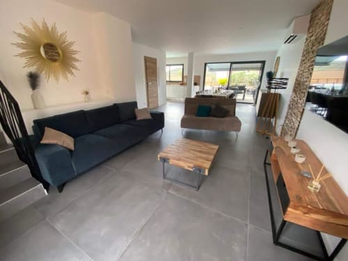 Modern living room in Villa Stella at Favone, with navy sofa, wooden table, and pool view doors, managed by Corsu di Core conciergerie