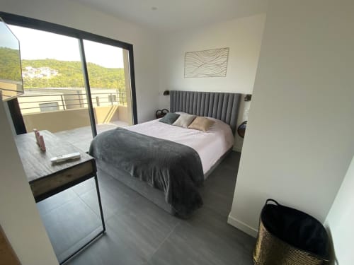 Modern bedroom in Villa Stella at Favone with gray upholstered bed, balcony view, and contemporary furnishings, managed by Corsu di Core conciergerie