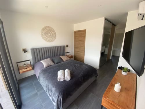 Modern bedroom in Villa Stella at Favone with gray upholstered bed, wooden furnishings, and flat-screen TV, managed by Corsu di Core conciergerie
