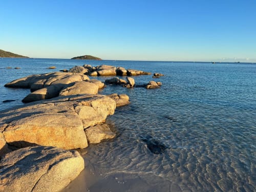 Golden granite rocks along pristine Favone beach in Corsica with clear blue Mediterranean waters and distant islands