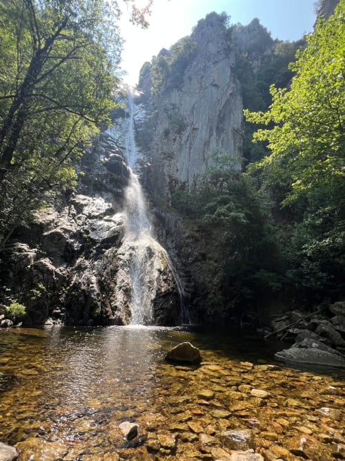 Waterfall cascading into emerald pool surrounded by limestone cliffs and lush greenery near Favone, Corsica