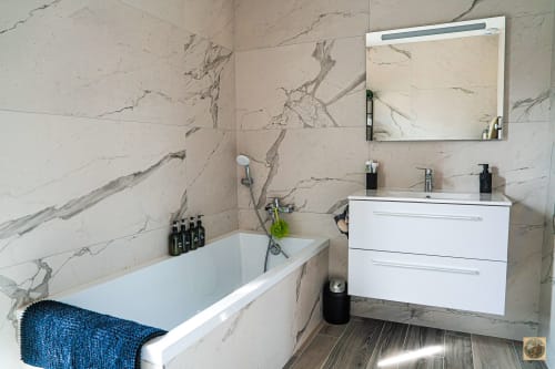 Salle de bain moderne avec carrelage en marbre, vanité blanche, miroir et baignoire blanche avec serviette bleue géré par la conciergerie Corsu di Core