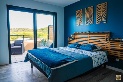 Chambre moderne aux murs bleu-vert, lit à structure bois, parure bleue, vue sur les collines depuis le balcon géré par la conciergerie Corsu di Core
