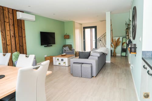 Salon moderne avec murs verts, canapé gris, téléviseur et coin repas géré par la conciergerie Corsu di Core