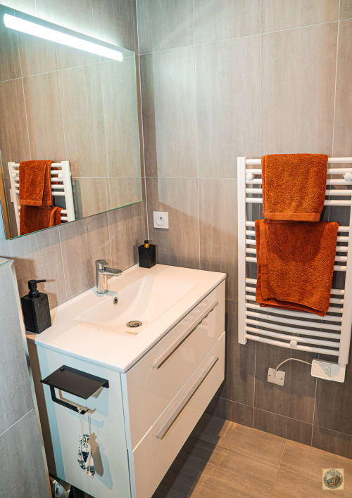 Salle de bain moderne avec vasque blanche, serviettes terracotta sur porte-serviettes chauffant, miroir éclairé géré par la conciergerie Corsu di Core