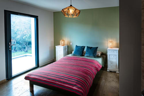 Chambre moderne à La Conciergerie du Cap Corse avec literie rayée rose, mur d'accent vert, luminaire géométrique suspendu, et
