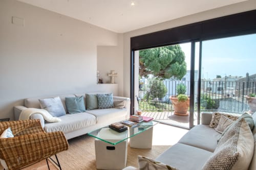 Elegant saló modern i lluminós amb sofàs blancs, taula de vidre i terrassa oberta amb vistes a Calella, Palafrugell