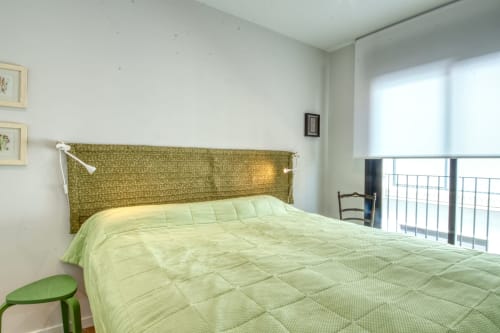 Dormitori lluminós en dúplex exclusiu de Finques Garcia Enrich, Palafrugell amb roba de llit acolchada verda i vistes a la ciutat