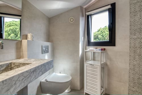 Bany modern en dúplex de Calella amb lavabo de marbre, vàter i finestra amb vistes a la vegetació