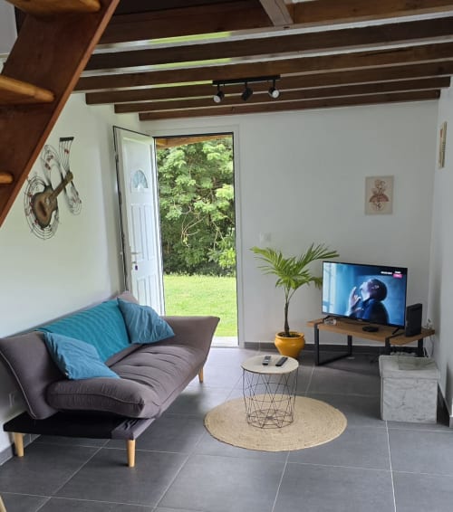 Salon moderne de la Villa Tourmaline avec canapé gris, téléviseur et vue sur le jardin par les baies vitrées au Lorrain