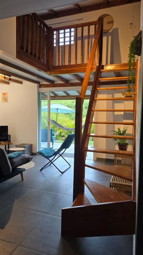 Mezzanine loft Villa Tourmaline avec échelle en bois, vue sur un jardin luxuriant et coin salon contemporain au Lorrain