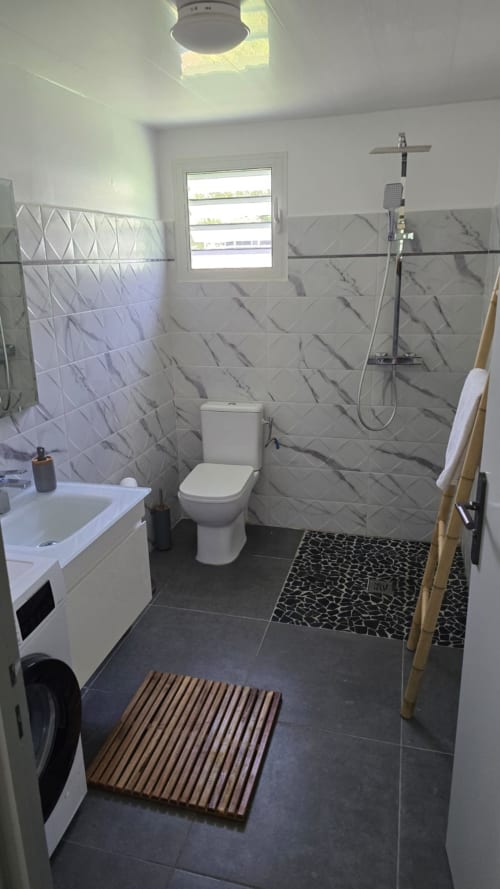 Salle de bain moderne à Villa Tourmaline avec carrelage effet marbre, douche à l'italienne, toilettes, lavabo et tapis de bain en bois à Le