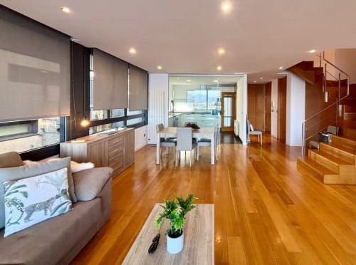 Moderno apartamento dúplex en Baiona con suelos de madera, vista al mar, cocina totalmente equipada, comedor y salón con sofá,