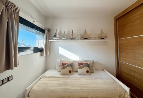 Luminoso dormitorio en apartamento de Baiona con vistas al mar, puerta de madera, decoración náutica de veleros y mobiliario temático costero