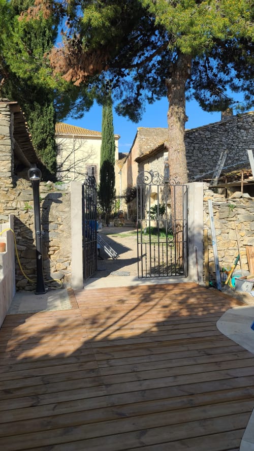 Portail en fer forgé de l'entrée de la piscine du N°9, cour en pierre avec cyprès et pins, Argeliers, France 