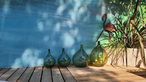 Terrasse piscine du N°9 Argeliers avec bouteilles vintage et plantes en pots sur sol en bois.