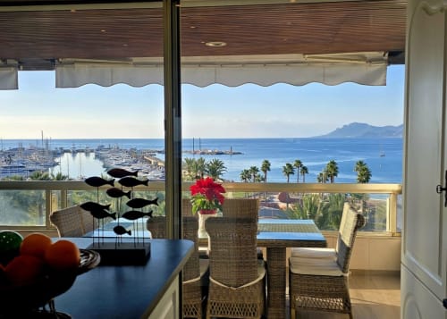 Balcone fronte mare con sedie in vimini, fiori rossi e veduta del Mediterraneo tra le palme a Campagnano di Roma