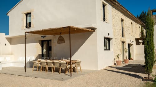 Cortile del Mas Lafleur a Châteaurenard con area pranzo ombreggiata, sedie in legno e edifici in pietra sotto cielo blu sereno