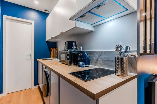 Modern kitchen in Bordeaux apartment with blue accent walls, wooden countertop, induction cooktop, and stainless steel