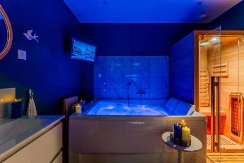 Luxury spa suite in Bordeaux with illuminated jacuzzi, sauna, blue ambient lighting, and wooden sauna room